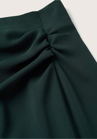 Tissu vert foncé avec des plis rassemblés créant des plis, mettant en valeur la texture et le détail du drapé.
