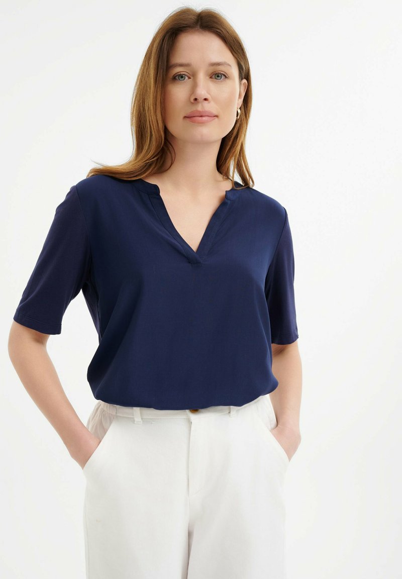 Navyblauw T-shirt met korte mouwen en een V-hals, gemaakt van gladde stof. Gecombineerd met witte hoge taillebroek met zijzakken.