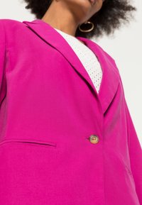 Blazer fucsia con design strutturato, chiusura con un solo bottone e rever elegante. Presenta una tasca laterale e una texture liscia.