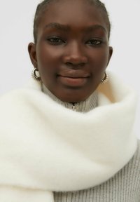 Weißer Fleece-Schal, der um den Hals gewickelt ist, mit weicher Textur, getragen über einem grauen Rippensweater mit hohem Kragen und Reißverschlussdetails.