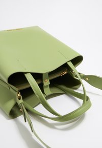Green leather tote bag with a zippered compartment, dual handles, and gold hardware accents. Smooth texture and minimalistic design.