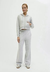 Lys grå cropped hettegenser med frontlomme og full glidelås, parret med lys grå vide joggebukser og sølvfargede joggesko.