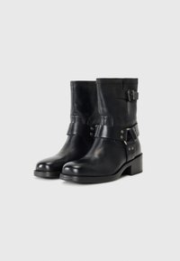 Botas de cuero negras hasta el tobillo con punta redonda, cierre de cremallera y correa decorativa con detalles de hardware. Tacón plano y robusto para mayor estabilidad.