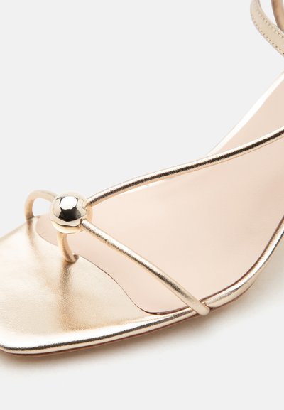 Sandale aurii cu bretele subțiri metalice și un mic bead sferic decorativ auriu lângă deget, cu partea din față deschisă, ascuțită.