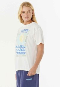 Camiseta blanca de cuello redondo con un diseño gráfico colorido que incluye el texto "ALOHA HOTEL", sol, olas y detalles de palmera. Corte casual.