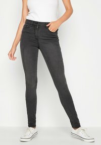 Musta farkku skinny-farkut sisältävät keski-navan vyötärön, viisi taskua ja hieman haalistusta rakenteen saamiseksi. Yhdistetty valkoisten lenkkarien kanssa.