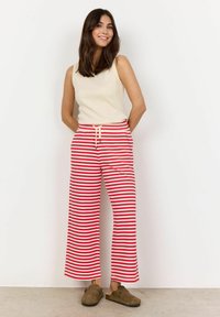 Pantalons larges rayés en rouge et blanc, avec une taille élastique et un cordon de serrage. Associés à un haut sans manches beige et des chaussures marron.