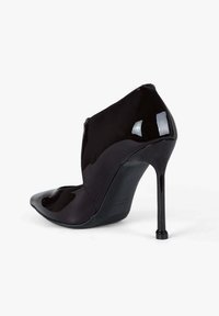 Scarpa con tacco alto in vernice nera, punta affilata e dettagli traforati, con una silhouette elegante e tacco a spillo.