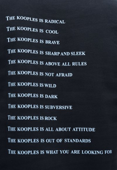 Μαύρο ύφασμα με επαναλαμβανόμενες λευκές φράσεις κειμένου που σχετίζονται με το brand "The Kooples", παρουσιάζοντας ποικίλες περιγραφές σε έντονη, μον τέρνα γραμματοσειρά.