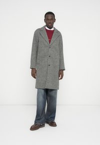 Pilko žvynelio rašto paltas su kampuotomis atlapomis, vienos eilės sagojimu ir dviem kišenėmis, derinamas su bordo spalvos megztiniu ir laisvų mėlynų džinsų.