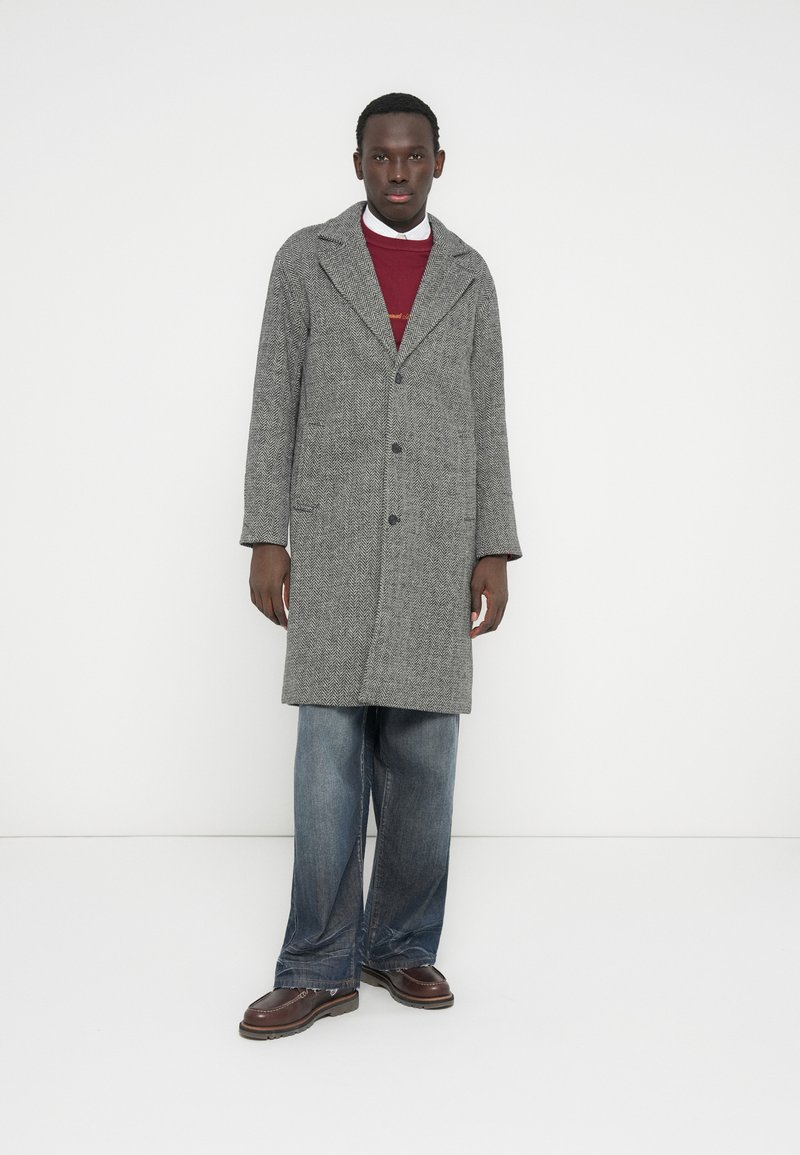 Pilko žvynelio rašto paltas su kampuotomis atlapomis, vienos eilės sagojimu ir dviem kišenėmis, derinamas su bordo spalvos megztiniu ir laisvų mėlynų džinsų.