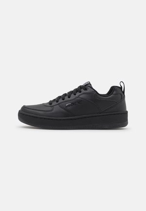 Czarny niski sneaker z zapięciem na sznurówki, teksturowaną skórzaną cholewką i grubą gumową podeszwą, pokazany z boku na białym tle.