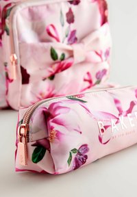 Pochette da trucco floreale in rosa con finitura lucida, dotata di zip in oro rosa e branding in rilievo "BAKER". Tessuto strutturato con motivi floreali vivaci.