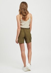 Pantaloni corti color khaki in tessuto testurizzato, con elastico in vita e tasche laterali, abbinati a una canotta di un leggero beige e sneakers bianche.