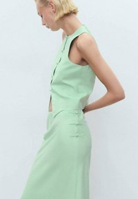 Robe sans manches vert menthe avec un corsage ajusté, découpes latérales et boutons décoratifs à la taille. Texture de tissu lisse et lignes épurées.