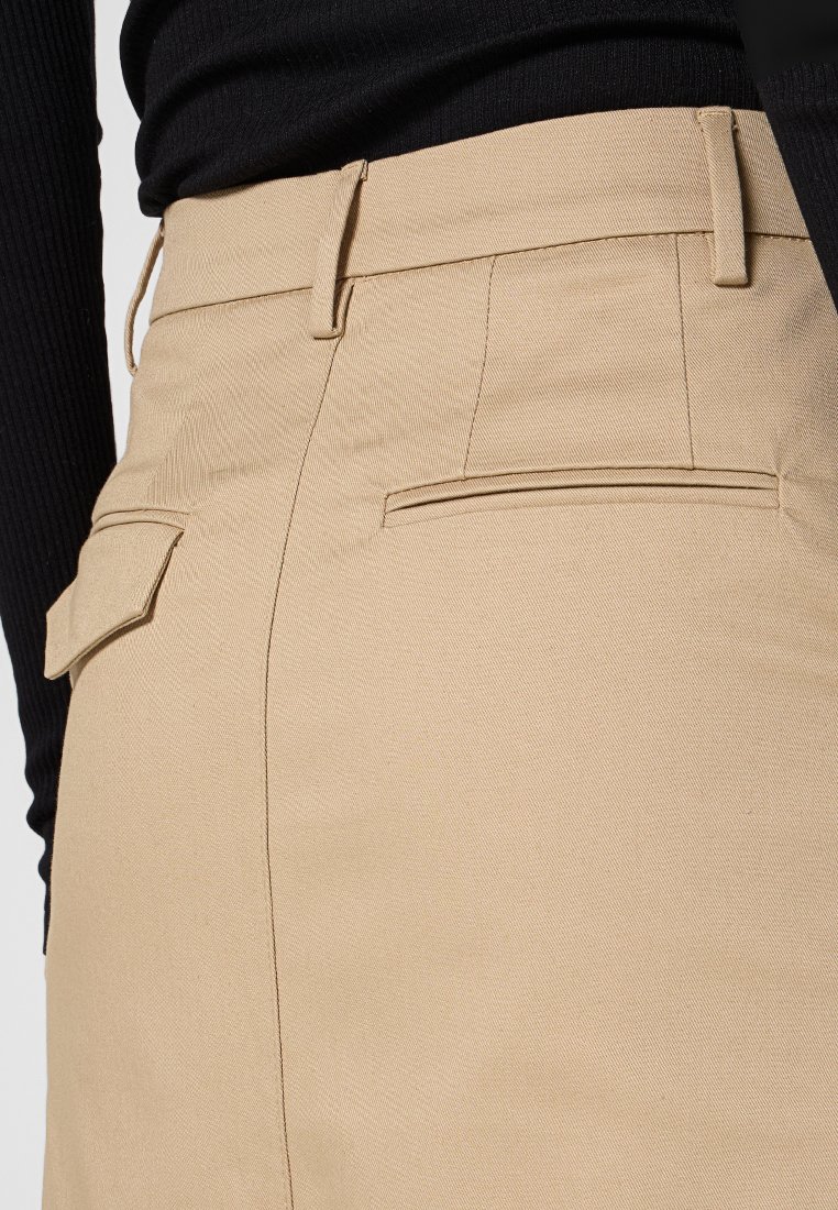 Beżowa spódnica z szlufkami na pasek i dwiema tylnymi kieszeniami, noszona z czarnym prążkowanym topem z długim rękawem.