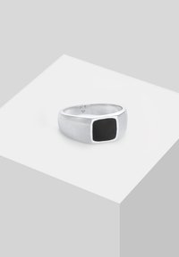 Hõbedane ring, millel on poleeritud pind, sisaldades ruudukujulist musta onixkivi, mis on paigutatud sujuvasse äärde. Lihtne geomeetriline disain.