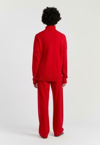 Maglione a collo alto rosso lavorato a maglia con spalle sagomate, abbinato a pantaloni a gamba larga. La consistenza morbida e la vestibilità rilassata aumentano il comfort.