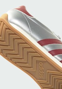 Silver synthetic sneaker with red accents and three side stripes. Textured gum rubber sole with a zigzag pattern, featuring brand logo.