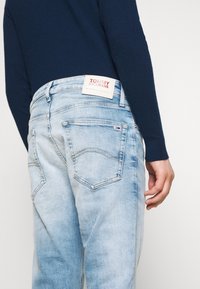 Ljusblå denimjeans med urblekta områden, bakfickor och en Tommy Jeans-etikett vid midjan. Jeans har en avslappnad passform.