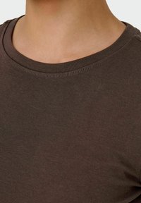 T-shirt a manica corta marrone con collo arrotondato, realizzato in cotone texture, che presenta un motivo a coste e dettagli cuciti vicino al colletto.