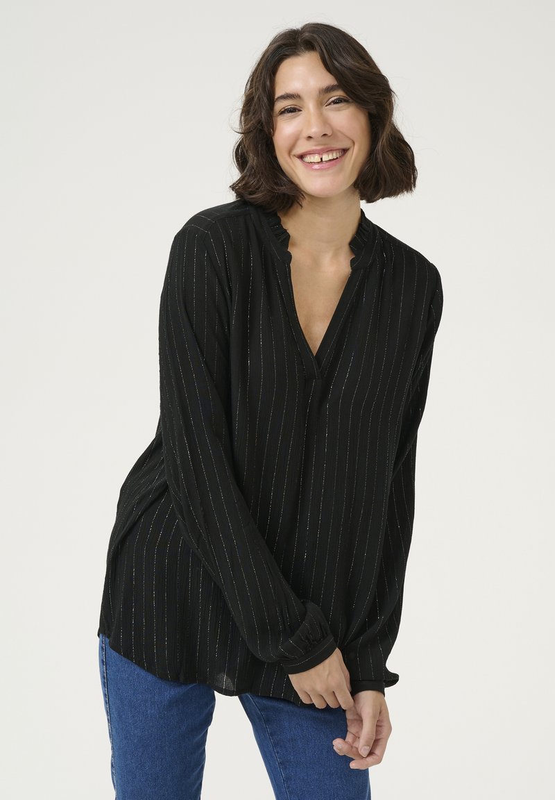 Blouse noire à manches longues avec des rayures verticales argentées, col volanté et coupe décontractée. Assortie à un jean en denim bleu.