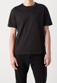 T-shirt nera a maniche corte in cotone con scollatura rotonda, caratterizzata da un piccolo logo sul petto e dettagli di cucitura discreti.