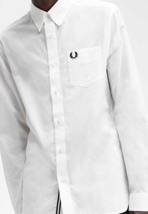Camicia bianca button-up realizzata in cotone morbido. Caratterizzata da una piccola tasca sul petto e da un emblema ricamato in nero sopra di essa.