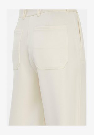 Zbliżenie kremowych spodni pokazujących tylne kieszenie z delikatnym przeszyciem i szlufkami na jednolitym tle.