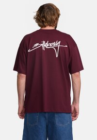 Bordó oversized tričko vyrobené z bavlny, s velkým bílým logem "Billabong" na zadní straně. Krátké rukávy a uvolněný střih.