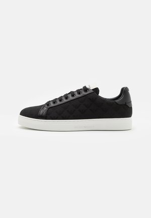 Zapatilla deportiva negra de perfil bajo con tela estampada, cordones negros y suela blanca grabada con el nombre de la marca.