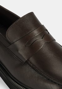 Bruine leren loafer met een stijlvolle, gladde oppervlakte, een asymmetrische band over de bovenkant en subtiele stiksels langs de naden.