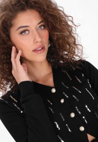 Schwarze Strickjacke mit Perlen- und Paillettenverzierungen, V-Ausschnitt, weichem Material und gerippten Bündchen.