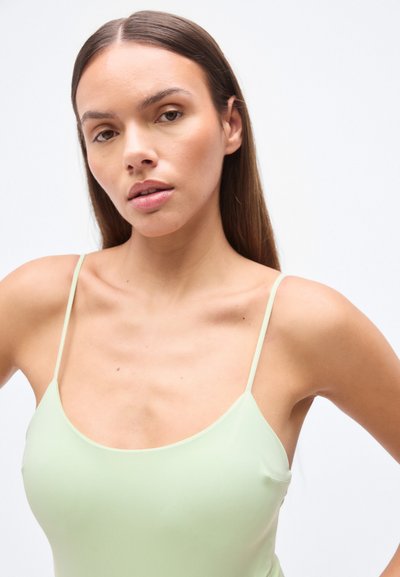 Ανοιχτό πράσινο, εφαρμοστό τοπ  με λεπτές τιράντες, με στρογγυλή λαιμόκοψη. Λείο ύφασμα και μινιμαλιστικός σχεδιασμός χωρίς ορατά μοτίβα.