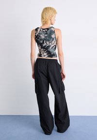 Svarte cargo bukser med store sidelommer, kombinert med en tettsittende, flerfarget tie-dye tank topp med rynket tekstur.