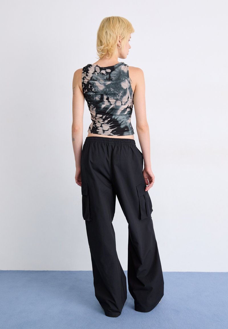 Pantalones cargo negros con grandes bolsillos laterales, combinados con una camiseta sin mangas de teñido anudado de múltiples tonos que presenta una textura fruncida.