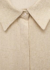 Beige button-up shirt with a textured woven fabric, featuring a classic collar and a single pearlescent button at the neck.