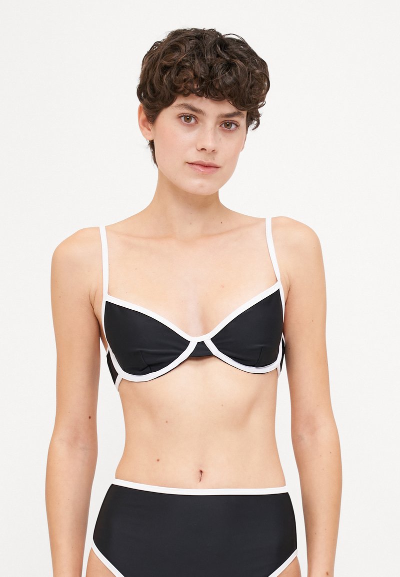 Fekete bikini fehér díszítéssel. Alulról támasztott pántos melltartó, állítható pántokkal és magas derekú alsó résszel rendelkezik. Simaság jellemzi, minimalista dizájnnal.