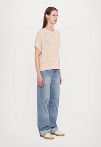 Lys ferskenfarget strikket genser med korte ermer, sammen med løse blå jeans med en subtil logo-print og beige sko.