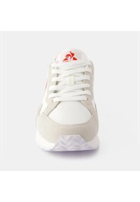 Sneaker bianca e grigia con una tomaia in suede e sintetico, caratterizzata da lacci bianchi, suola stampata e un logo rosso sulla linguetta.