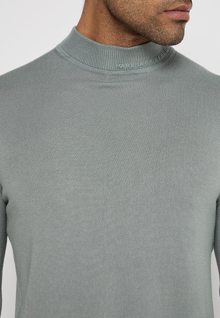 Hellgrüner Pullover mit hohem Kragen aus strukturiertem Strickstoff. Besitzt ein dezentes Logo am Kragen und ein figurbetontes Design.