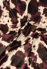 Μεταξένιο ύφασμα με αφηρημένο ζωικό μοτίβο σε εκρού, σκούρο καφέ και μοβ, απαλά διπλωμένο δημιουργώντας μαλακές σκιές και φωτεινές ανταύγειες.