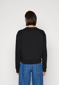 Černá mikina s kulatým výstřihem, žebrovanými manžetami a lemem. Vyrobena z měkké látky, má volný střih a minimalistický design.