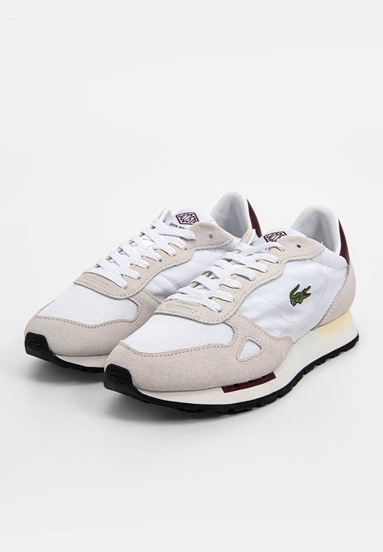 Zapatillas blancas y beiges con parte superior de ante y malla, que presentan un logo verde, cordones en tono y una suela de goma negra.