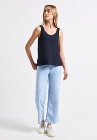 Top senza maniche blu navy con spalline arricciate, abbinato a jeans a gamba larga azzurri chiari con uno spacco frontale. Sneakers bianche completano il look.