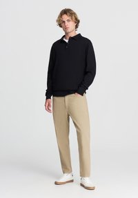 Polo a maniche lunghe nera con colletto, pantaloni beige a gamba dritta e sneakers bianche. Tessuto morbido con una vestibilità comoda e dettagli sottili.