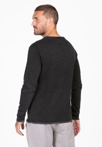 Zwart langslavend shirt van zachte stof met een ronde hals, schone naden en een relaxte pasvorm. Geen zichtbare branding of patronen.