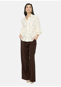 Camicia button-up crema con motivo a occhiello aperto, maniche lunghe, abbinata a pantaloni ampi marroni e tacchi neutri. Design semplice ed elegante.