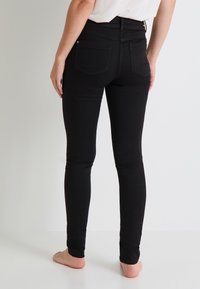 Jeans skinny negros hechos de una tela elástica, con una cintura alta, dos bolsillos traseros y una textura lisa y suave.