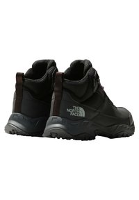 Botas de senderismo impermeables negras con parte superior texturizada, cuello acolchado, suela de goma y lengüetas de agarre. Presenta un logo reflector en el lateral.